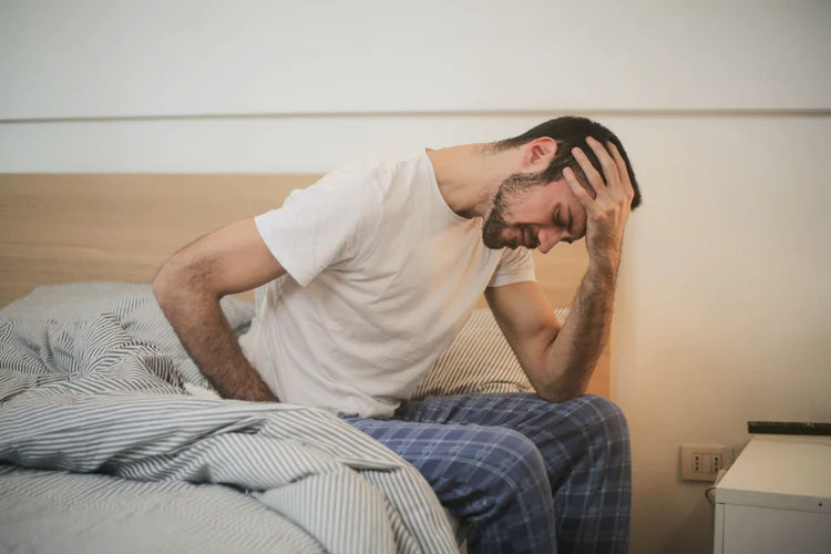 Fiatal férfi az ágy szélén fájdalmasan ül. A lumbágó kellemetlen gerincbetegség.